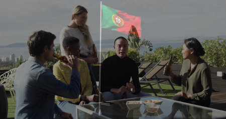 Socializing five friends sitting around coffee table with beers on rooftop terrace, Portuguese flag. Friends, socializing, rooftop, modern, leisure, urban, celebrationの写真素材