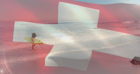 Standing woman surfer holding yellow surfboard in shallow surf at sandy beach, Swiss cross overlay. Beach, surfing, coastline, adventure, serenity, sport, summerの写真素材