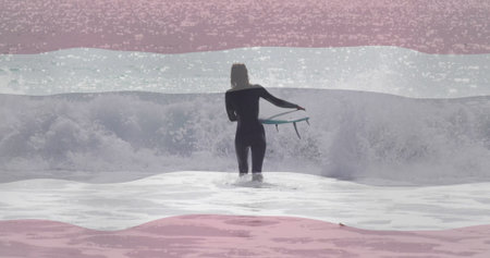 Standing female surfer wearing wetsuit holding short surfboard in ocean surf, with breaking waves. Adventure, aquatic, sport, athleticism, active, seaside, landscapeの写真素材