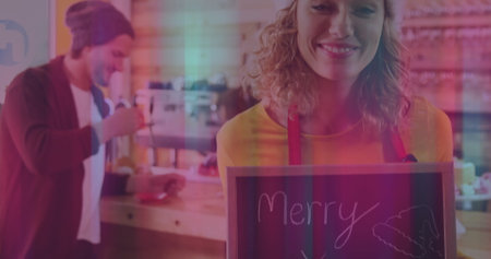Holding Merry chalkboard sign, smiling barista in red apron at cafe counter, copy space. Cafe, hospitality, warm, festive, cheerful, rustic, teamworkの写真素材