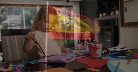 Girl in short-sleeve shirt painting paper at home, with paintbrush scissors Spanish flag overlay. Children, artistry, creativity, home environment, crafting, colorful, educationalの写真素材