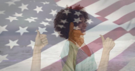 Smiling woman wearing green top giving thumbs up in coastal double exposure, with US flag overlay. Celebration, optimism, patriotism, adventure, empowerment, serenity, patrioticの写真素材