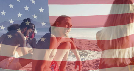 Laughing man in red swim trunks sitting on sandy shoreline, with translucent American flag overlay. Beach, shoreline, ocean, leisure, friendship, sunny, relaxationの写真素材