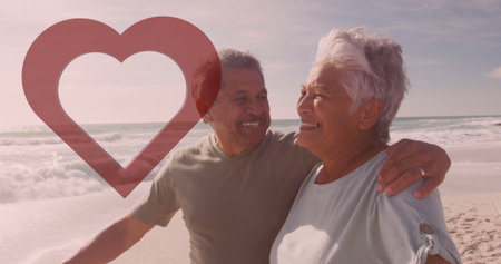 Strolling senior couple along sandy shoreline, with gentle waves and red heart graphic overlay. Romance, aging, coastal, leisure, serenity, naturist, companionshipの写真素材