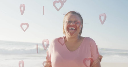 Laughing senior woman wearing pink shirt on sandy beach shoreline, with digital heart overlays. Joy, bliss, relaxation, vitality, serenity, happiness, outdoorの写真素材