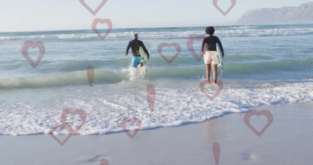 Walking surfers in rash guards carrying surfboards into ocean waves at sandy shore, with mountains....