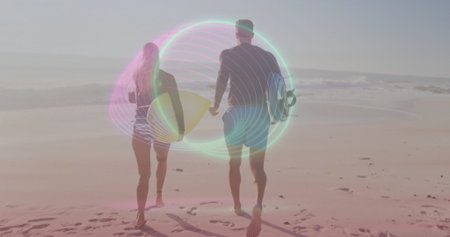 Walking two surfers wearing wetsuits and board shorts on beach, with surfboards and footprints....