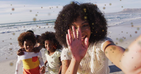 Taking selfie woman with curly hair wearing white top capturing family at beach, with smartphone. Family, shoreline, vacation, leisure, sunny, outdoor, candidの写真素材
