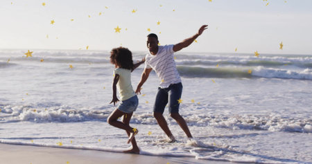 Running father and daughter splashing in shallow ocean surf on sandy shore, with golden star shapes....