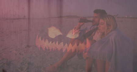 Sipping couple wrapped in fringed blanket sitting on beach at dusk, with dark glass bottles....