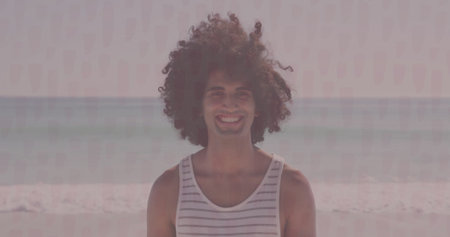 Standing man wearing striped tank top at beach shoreline, with gentle ocean waves behind. Outdoor,...