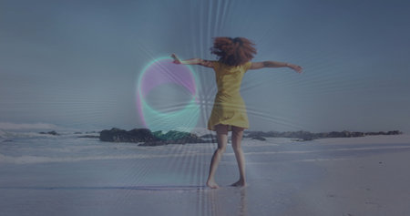 Spinning woman in yellow sundress dancing on wet sand at beach shoreline, with dark rock formations....