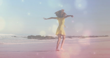 Spinning African American female dancing near water's edge on sandy beach, with yellow dress. Joy,...