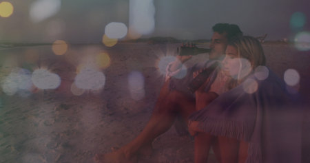 Sipping couple wrapped in fringed throw blanket on beach at dusk, with glass bottles, copy space. Romantic, serenity, dusk, leisure, intimacy, twilight, dreamyの写真素材
