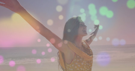 Spreading arms woman wearing yellow floral dress standing on beach shore, with colored light spots. Carefree, serenity, summer, tranquility, outdoor, vitality, bohoの写真素材