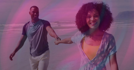 Walking couple holding hands along wet sand by ocean, wearing henley shirt and floral beach dress....