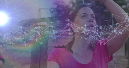 Leaning woman in pink shirt raising hand above head at park, with fence and water droplets. Fitness,...