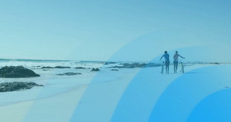 Walking couple in sportswear pushing bicycles along beach with rocks and lapping waves, copy space....