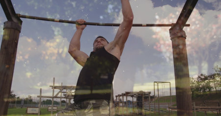 Gripping pull-up bar, fit man pulling body upward at fitness park, wearing camouflage shorts....