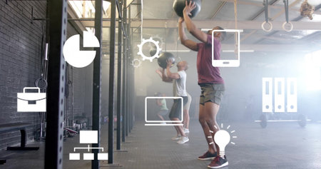 Throwing man wearing maroon tee performing wall ball throws at warehouse gym with medicine balls. Fitness, workout, training, strength, exercise, athletic, sportsの写真素材