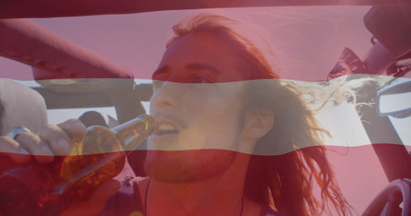 Raising male passenger drinking from brown glass bottle in convertible car, wind blowing hair back. Adventure, freedom, lifestyle, outdoor, travel, motion, vibrantの写真素材