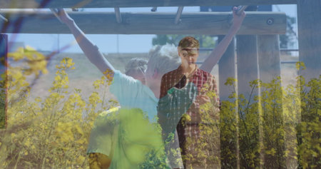 Hanging boy holding onto wooden monkey bars at park playground, with yellow wildflowers blooming. Outdoor, activity, adventure, playful, nature, family, vibrantの写真素材