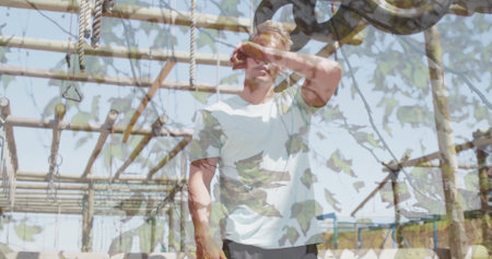 Raising forearm, man wiping sweat at outdoor obstacle course, with beams ropes rings pulley wheel. Adventure, fitness, strength, outdoor, athleticism, training, enduranceの写真素材