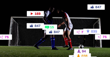 Players wearing blue-red kits racing for ball on pitch at night, with goal net and overlays. Action, competition, teamwork, athleticism, sport, entertainment, digitalの写真素材