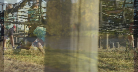 Guiding instructor leading group of children crawling under low rope net on grassy course with logs....