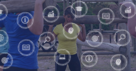 Woman in yellow top carrying log and navigating obstacle course in dirt clearing with digital icons....