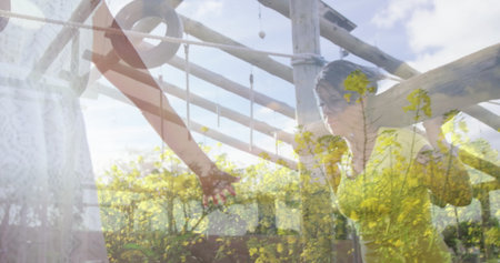 Gripping woman in sleeveless top raising arms under pergola beams, with ropes and yellow flowers. Vineyard, friendship, leisure, rustic, bohemian, nature, wellnessの写真素材