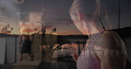 Lifting dumbbell, female exerciser training inside gym area, with lakeside sunset overlay and reeds....