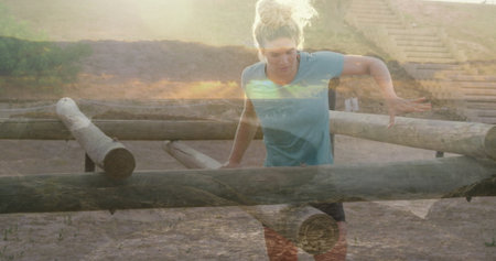 Negotiating light-skinned woman jumping low wooden logs barrier on sandy course, with wooden steps. Adventure, outdoor fitness, active lifestyle, training, endurance, athleticism, natural environmentの写真素材