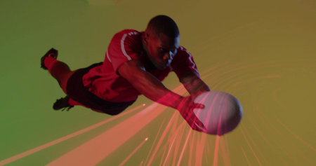 Diving athlete in red jersey, black shorts catching white ball in studio, with red light trails. Dynamic, action, motion, competition, strength, agility, vibrantの写真素材
