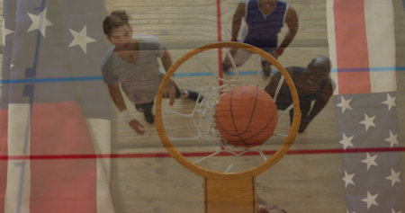 Dropping orange basketball through net at gym, with athletes reaching under American flag overlay. Athletics, teamwork, competitive, energetic, amateur, sport, gymnasiumの写真素材