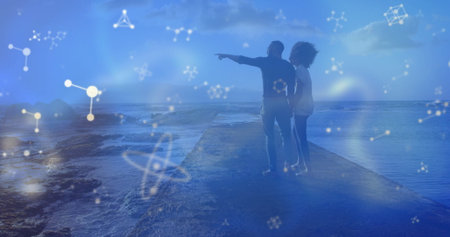 Standing couple pointing at horizon at jetty end, glowing constellation and molecular shapes. Romantic, exploration, adventure, serenity, cosmic, innovative, natureの写真素材