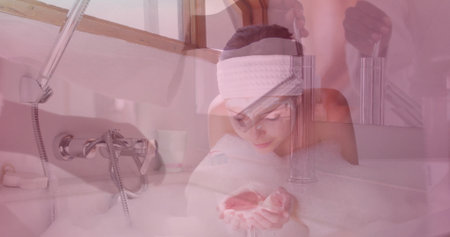 Leaning woman wearing spa headband cupping water over foam tub by skylight, with faucet and mug. Relaxation, wellness, self-care, spa, tranquility, bathroom, soothingの写真素材