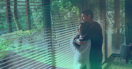 Embracing couple wearing sweater and jeans at home and gazing through window blinds, copy space. Romantic, intimacy, tranquility, architecture, natural light, minimalism, leisureの写真素材