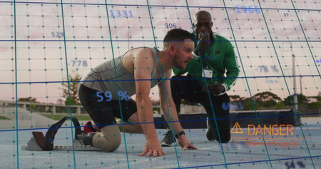 Crouching amputee runner using blade at blocks on track, with coach using device overlaying danger....