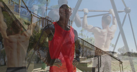 Man in red top, black sleeves with crossbody strap supervising pull-ups on beach, with metal bars....
