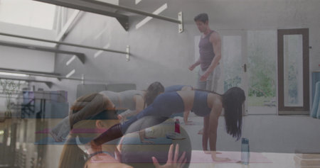 Five participants wearing sportswear planking while following instructor in studio, with yoga mats....