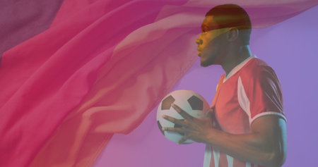 Soccer player wearing red jersey holding soccer ball in studio, with floating fabric, copy space. Athlete, sportswear, dynamic, vibrant, motion, energy, modernの写真素材