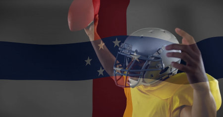 Helmeted yellow-jerseyed football player holding football in studio, flag overlay, copy space. Athlete, sportsgear, patriotism, victory, determination, dynamic, energeticの写真素材