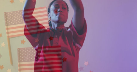 Woman in red polo shirt and glasses raising arms overhead in studio, with American flags, stars. Patriotism, celebration, empowerment, festive, vibrant, confident, unityの写真素材