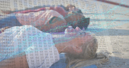 Sunbathing two women lying on sandy shoreline, with blue beach towels, swimsuits and data overlay....