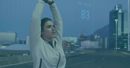 Stretching athlete wearing jacket raising arms overhead on bridge at dusk with biometric metrics. Fitness, urban, technology, vitality, health, performance, activewearの写真素材