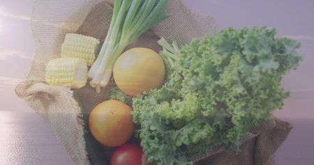 Burlap sack lined with green cloth resting on wooden dock by calm water, with fresh vegetables. Rustic, harvest, vibrant, outdoor, natural, countryside, compositionの写真素材