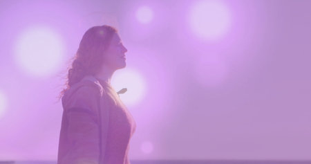 Gazing woman wearing light jacket and textured sweater on shoreline at dusk, with pastel sky flares. Serenity, contemplation, twilight, minimalist, nature, tranquility, aestheticの写真素材