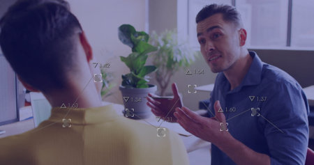 Man in blue shirt gesturing and explaining data overlays in office, with dual monitors, copy space....
