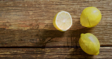 Displaying three yellow lemons resting on table planks under sunlit foliage shadows, copy space. Citrus, produce, rustic, natural, vibrant, healthy, farm-freshの写真素材
